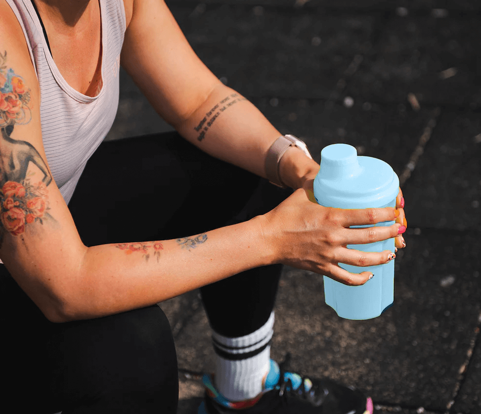 Woman in the gym holds Fiteg2 protein shaker 700 ml | Sieviete sporta zālē ar Fiteg2 proteīna šeikeri 700 ml